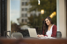 a young woman sitting at a table outdoors working at a laptop computer 
