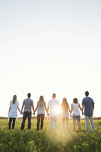 group of young adults standing outdoors holding hands in prayer