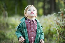 a toddler boy outdoors in a jacket looking up