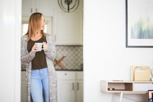 a woman with a coffee cup standing in a kitchen 
