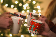 Christmas cups with hot cocoa and candy canes are  put together to make a toast.