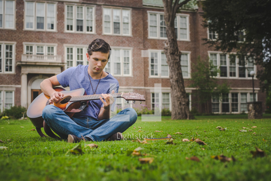 young man sitting in grass playing a guitar 