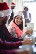 A woman in a santa hat smiling and drinking coffee
