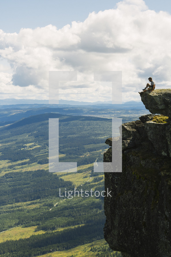 a man sitting on the edge of a cliff looking out over the valley below 