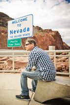 man sitting in front of a Welcome to Nevada sign