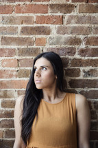 A young woman sitting against a brick wall.