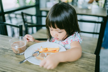 a toddler girl eating and playing with her food at a restaurant 