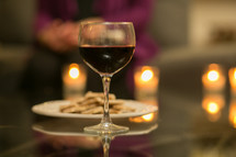 Glass of wine and a plate of crackers on a mirrored table with lit candles.