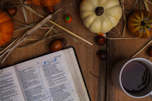 Holy Bible on a wood table surrounded by pumpkins and coffee mug 