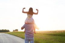 a daughter on her father's shoulders showing her muscles 