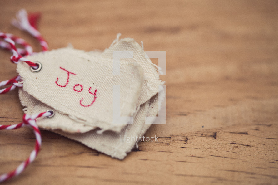 A stack of Christmas gift tags, the top one labeled "Joy", on a wood table.