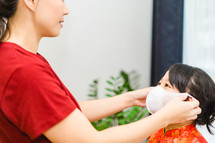 a mother helping a child put on a face mask 