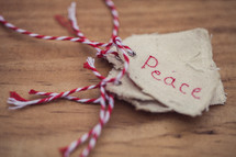 A stack of fabric Christmas gift tags, the top one labeled "Peace," on a wood grain background.