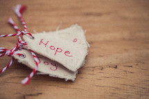A stack of Christmas gift tags, the top one reading "Hope," on a wood grain background.