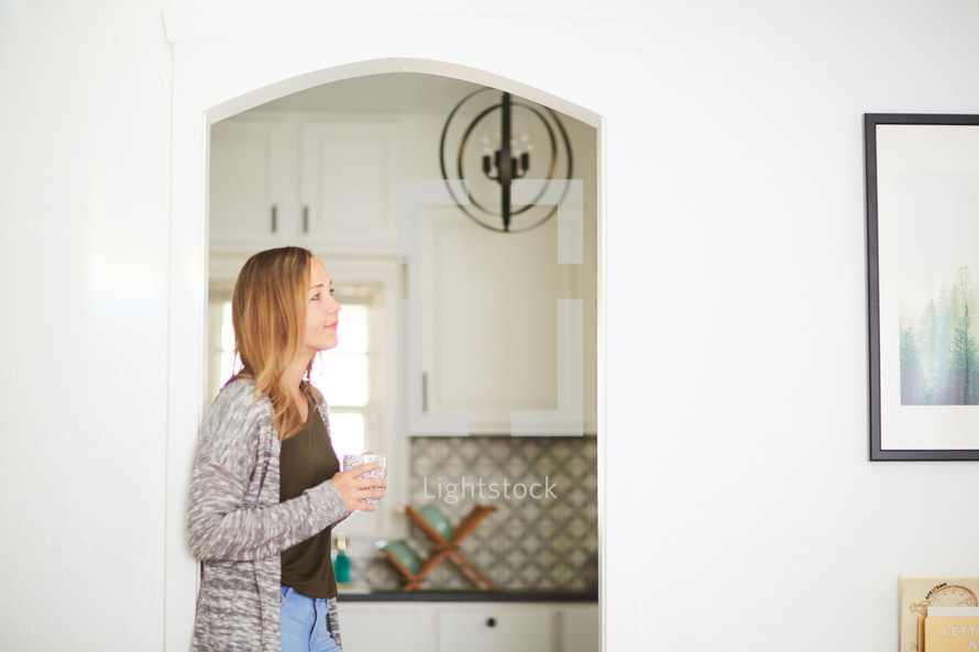 a woman standing in a kitchen with a coffee mug 