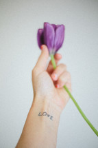 Hand holding a tulip flower; "love" tattooed on the wrist.