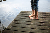 Feet standing on a wooden pier on a lake.
