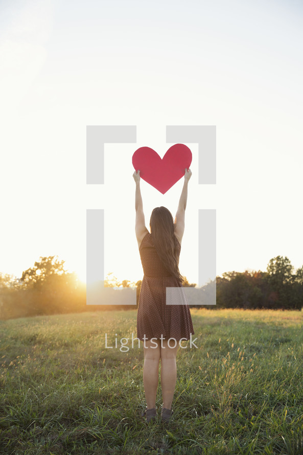 woman holding up a paper heart at sunset 