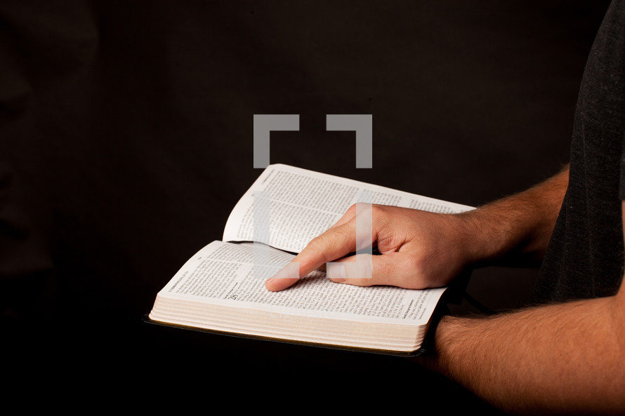 a man with his finger on scripture on the pages of a Bible 