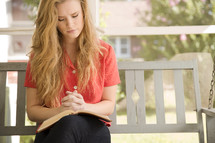 woman sitting on a porch swing praying with a Bible in her lap 
