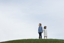sisters standing on a hilltop holding hands 
