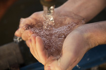 cupped hands holding water from a spigot 