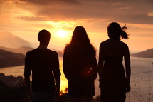 Silhouette of friends standing outside overlooking the ocean at sunset.