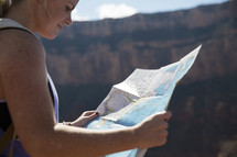 woman standing at the edge of a canyon cliff reading a map 