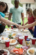 holding hands in prayer above a table at a cookout 