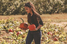 girl child picking out a pumpkin in a pumpkin patch 