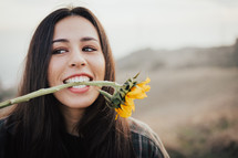 a woman with a sunflower between her teeth 