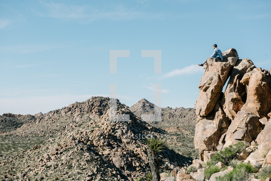 a man sitting on a rock looking out at a desert 