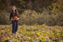 girl child picking out a pumpkin in a pumpkin patch 
