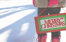 a woman in the snow holding a Merry Christmas sign