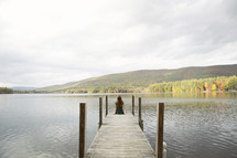 woman sitting at the end of a dock over a lake 