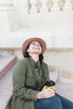 Portrait of a woman sitting on the steps of a building smiling and holding a to-go coffee cup.