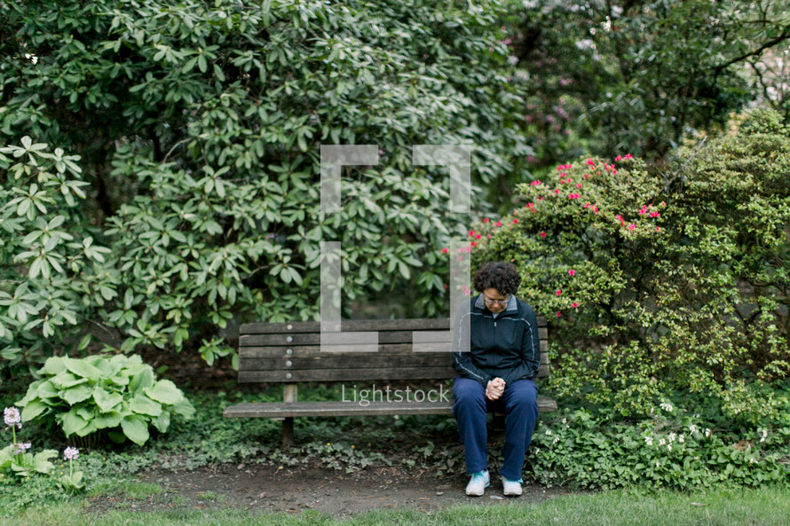 a woman sitting on a park bench praying 