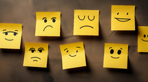 Sad and happy faces drawn on yellow sticky notes. 