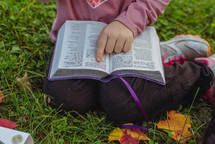 a child reading a Bible outdoors 