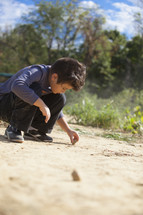 boy child drawing in sand with a rock 