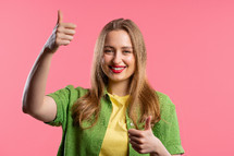 Stylish woman with hand sign like, thumbs up gesture. Happy lady, correct perfect choice, great deal, pink background. Positive female model smiles to camera, approval, trust concept.
