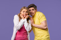 Frightened white american couple afraid of something and looks into camera with big eyes full of horror on violet wall background. Blonde woman and man. High quality 