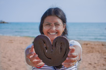 a smiling woman on a beach holding a heart 