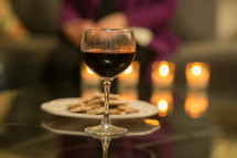 Glass of wine and a plate of crackers on a mirrored table with lit candles.