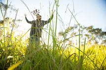 man standing outdoors in tall grass with raised arms 