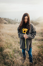 a woman standing outdoors holding a bouquet of sunflowers 