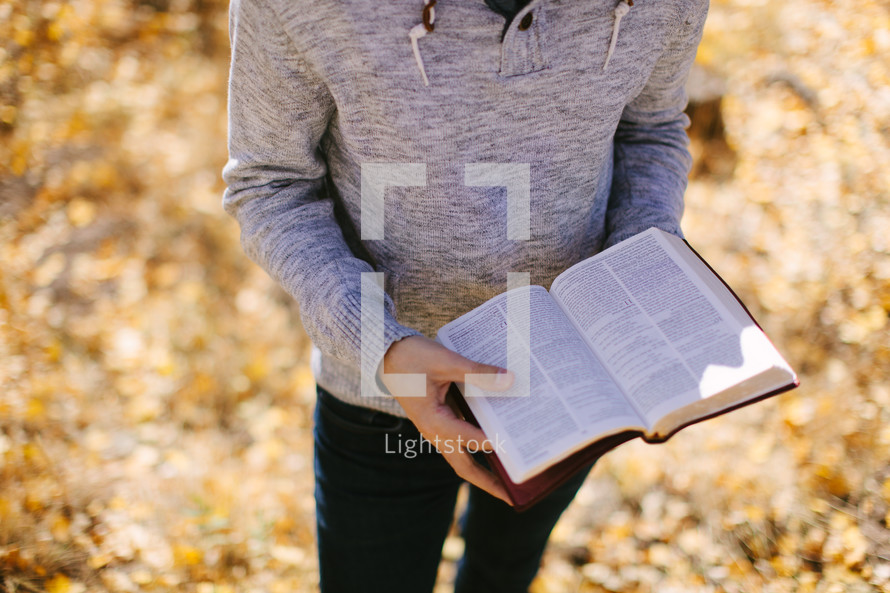 man standing holding a Bible in fall leaves 