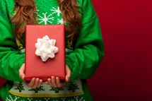 a woman in a Christmas sweater holding a wrapped gift 
