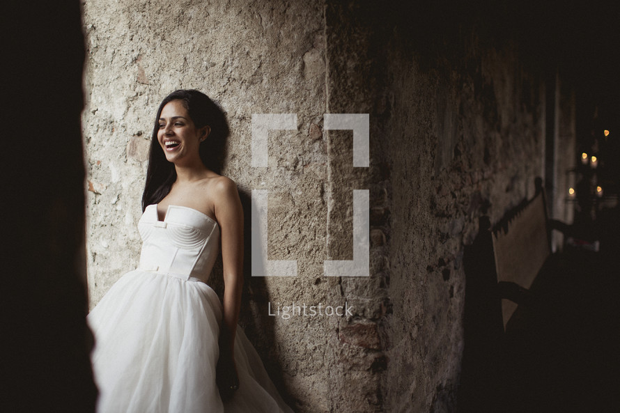 Bride smiling, leaning against a stone wall