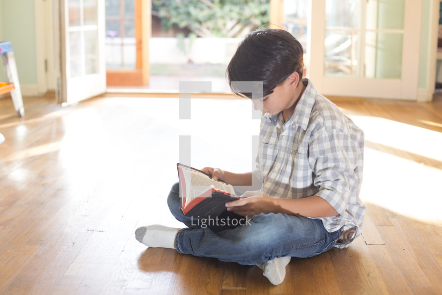A child sitting on the floor and reading the Bible.